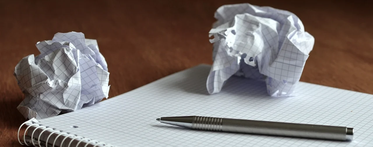 A pen lying on a blank notepad, with two screwed-up balls of paper visible